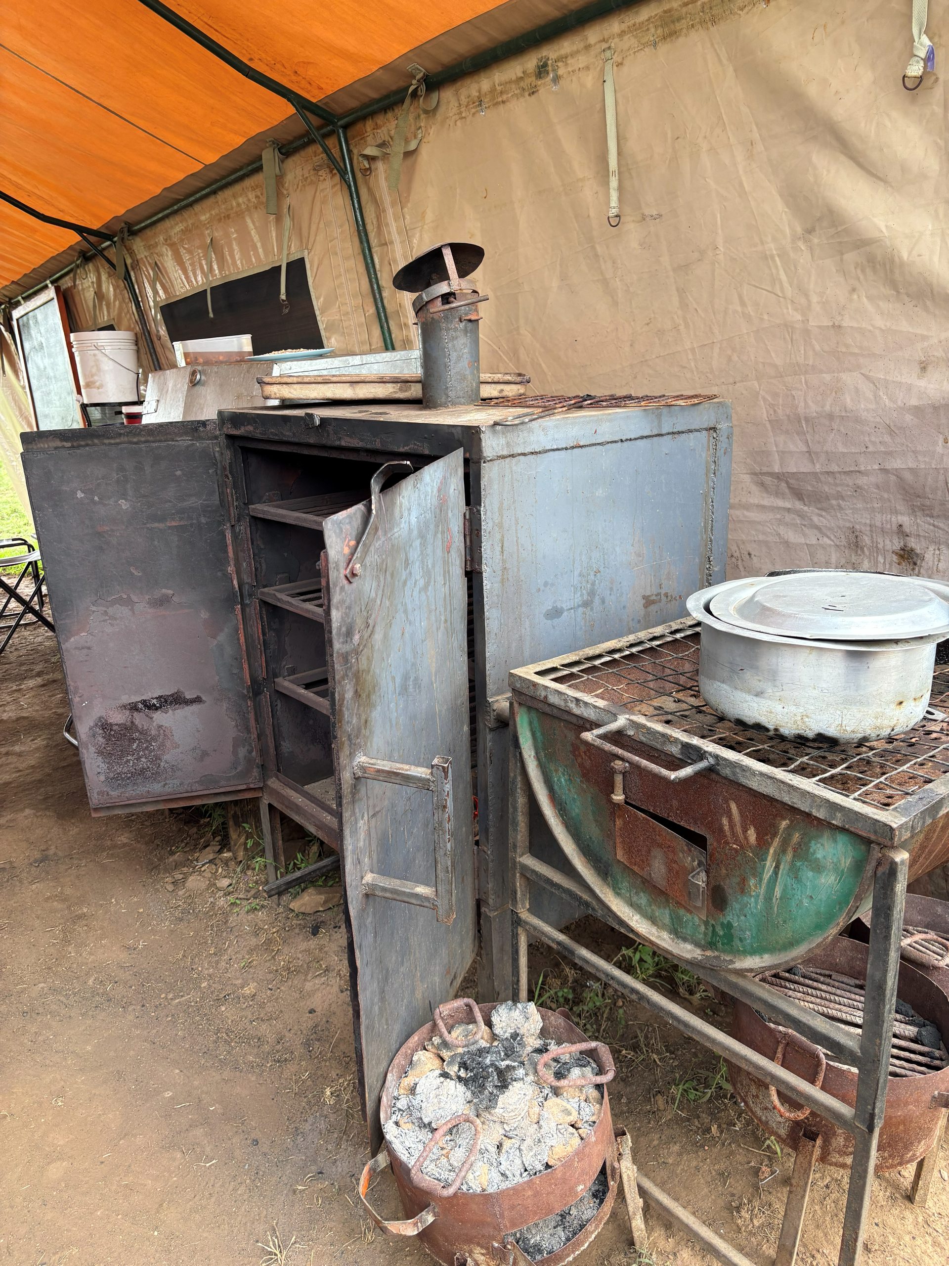The Nyumba camp kitchen — a heavy iron wood-fired oven with chimney and a charcoal brazier, inside the orange-roofed kitchen tent