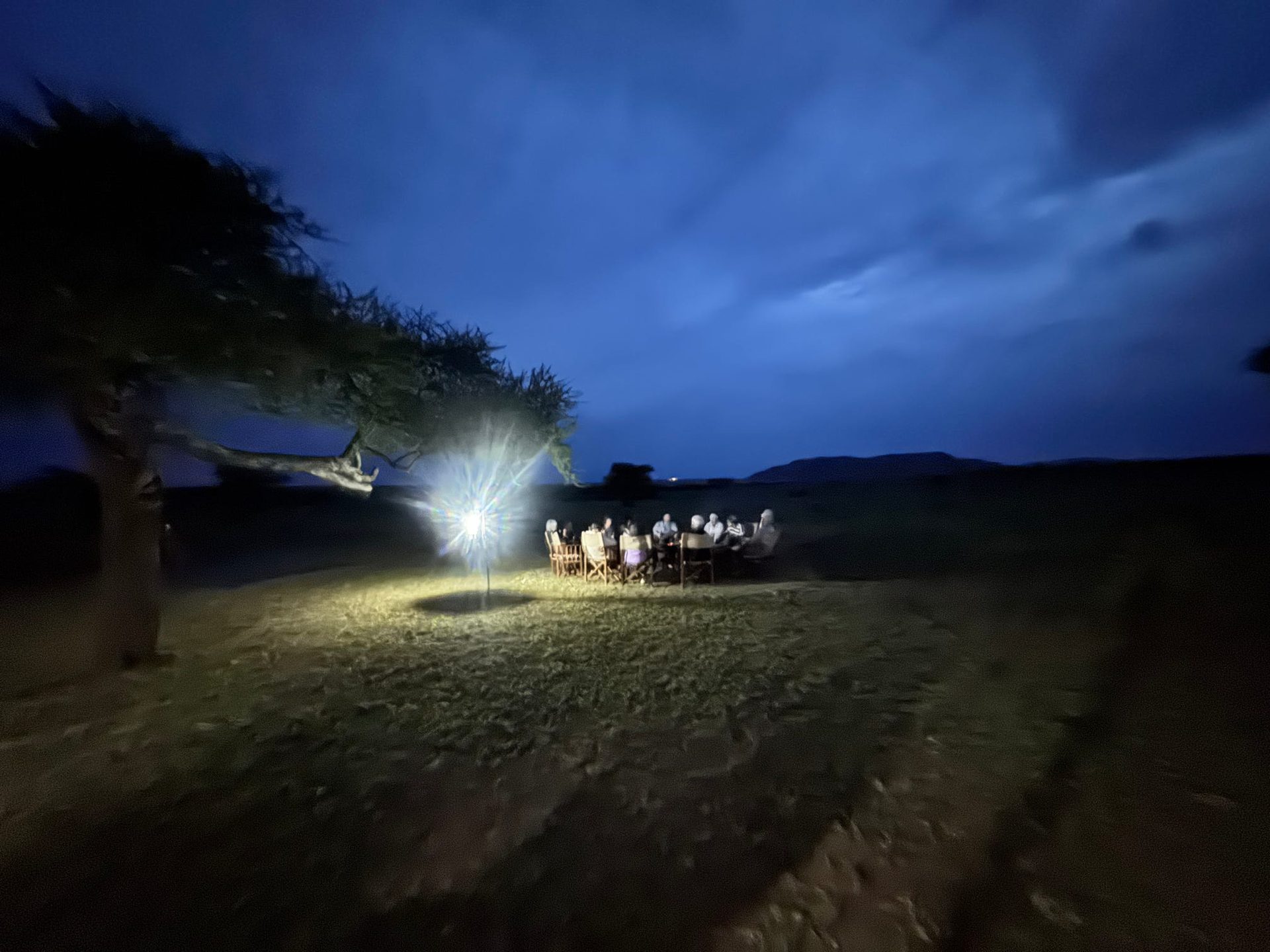 Group dining under a single lantern in the open Tarangire plains at night