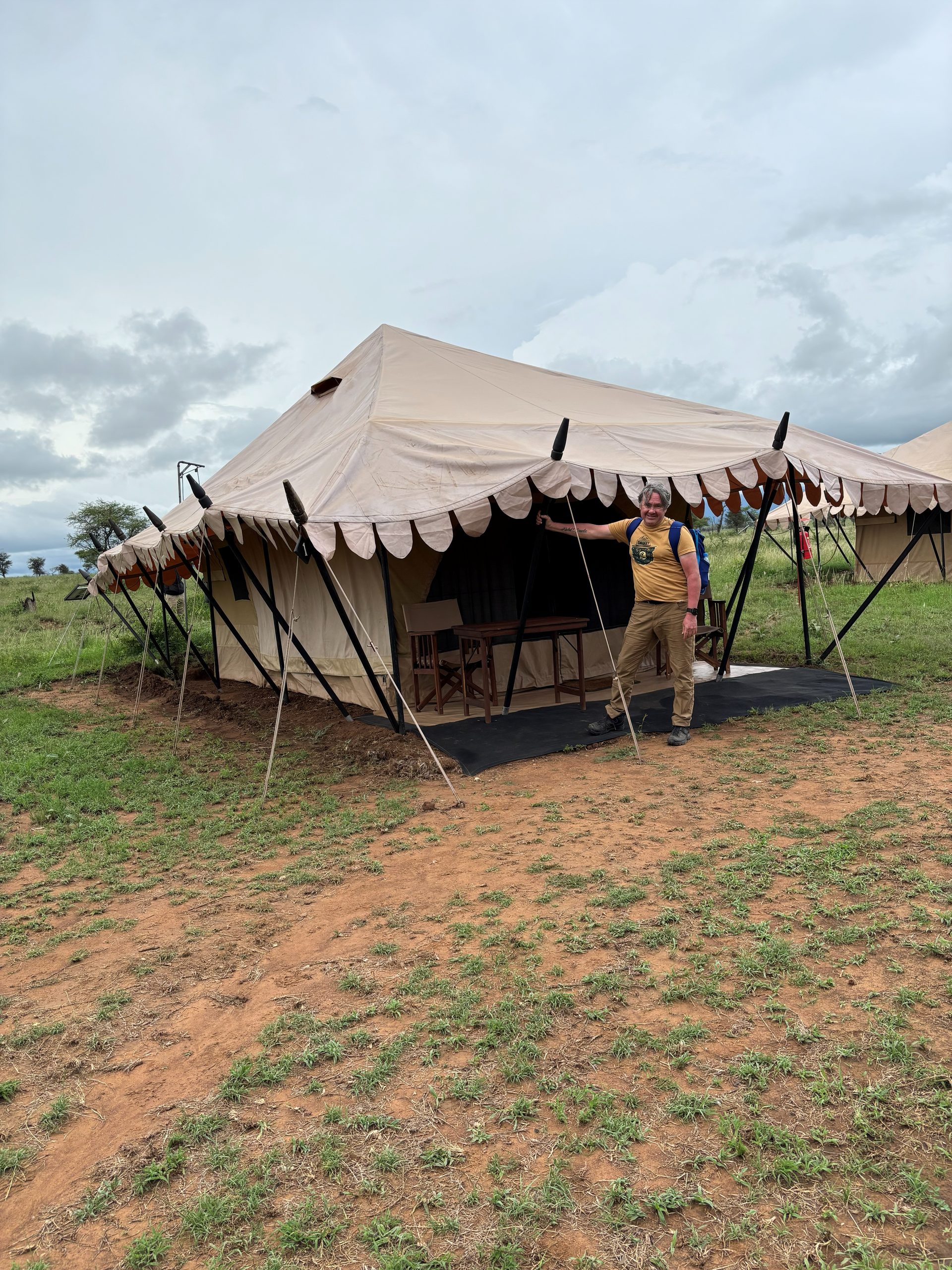 Robert standing at the entrance of his Nyumba tent, pointing at the door — the Serengeti plain stretching away behind